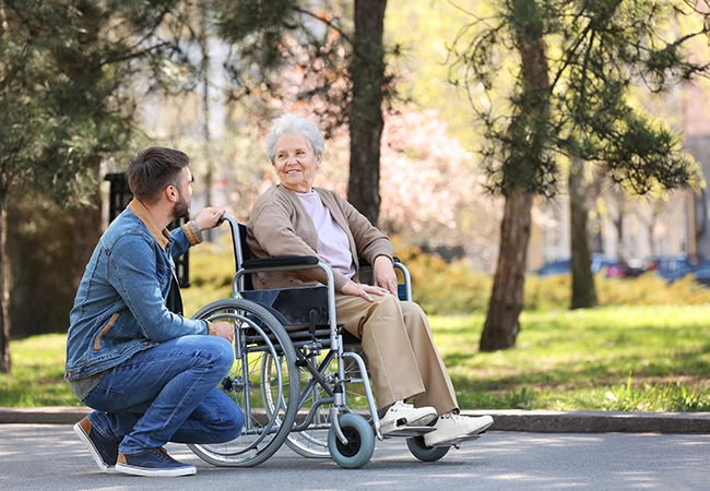 Image of woman standing next to a man sitting in a wheelchair at the beach Image of man kneeling next to woman sitting in a wheelchair